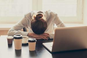 Umorna žena spava za stolom u uredu, okružena kavama
